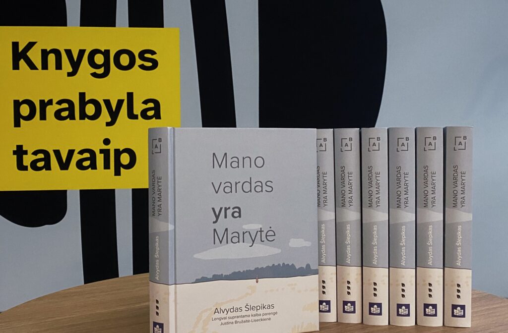 Greta ant stalo surikiuotos šešios spausdintos knygos „Mano vardas yra Marytė“. Už jų – užrašas su bibliotekos šūkiu: Knygos prabyla tavaip.