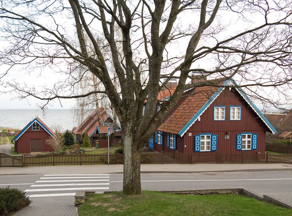 Gatvės vaizdas Kuršių nerijoje su autentiška medine žvejo sodyba, esančia netoli marių kranto.