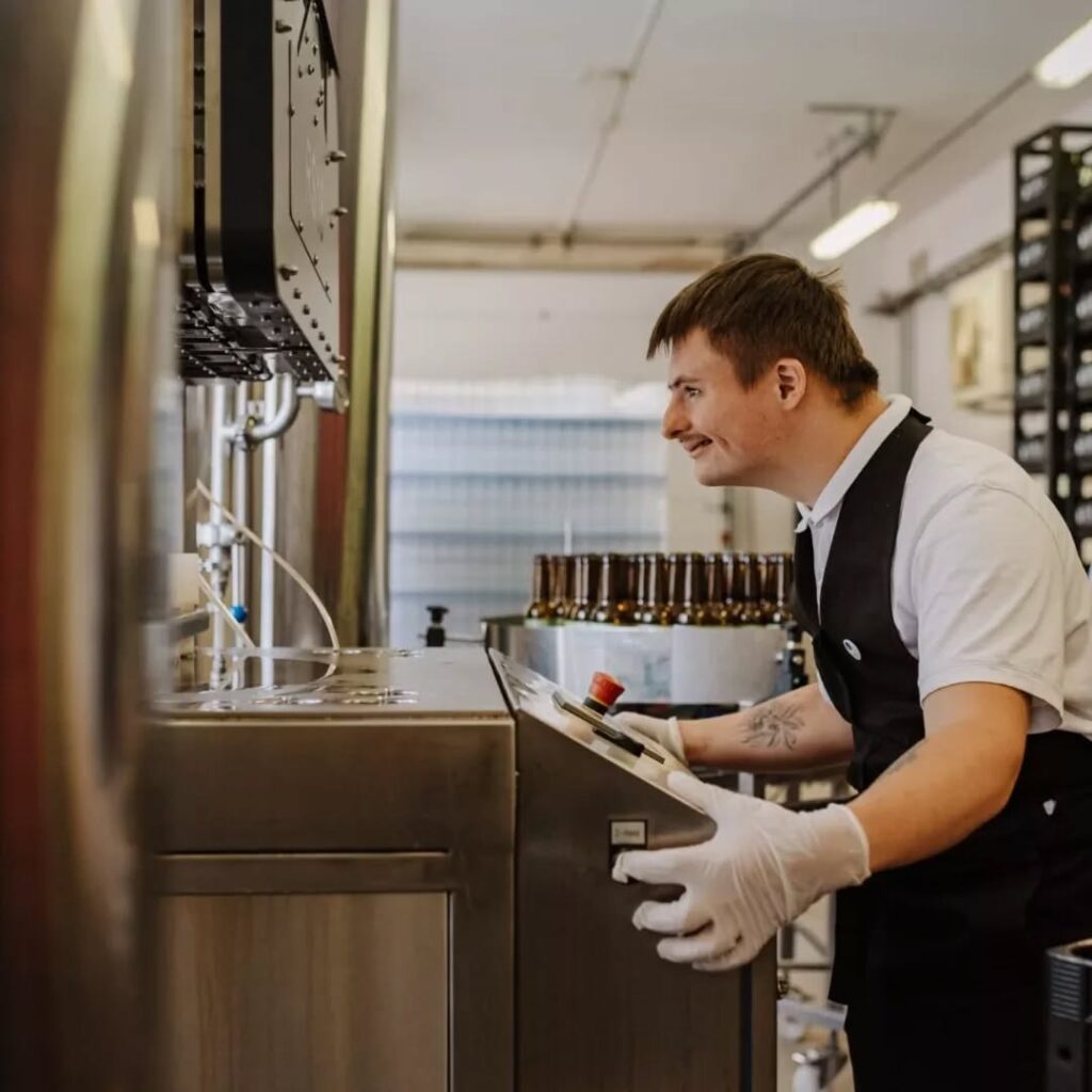 Reklamos herojus darbo vietoje. Vaikinas stovi šalia didelio mechaninio įrenginio.