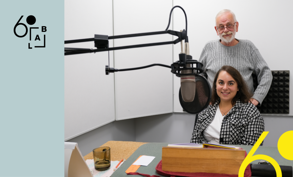 Garso įrašų studijoje prie mikrofono sėdi diktorė Gustė Pupkevičienė, už jos stovi kolega Algimantas Butvilas. Iliustraciją puošia LAB60 logotipas ir geltoni grafiniai akcentai, atkartojantys logotipą.