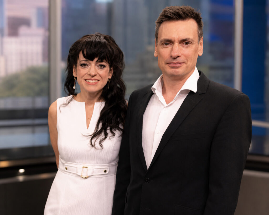 Šalia stovi ir šypsosi vyras tamsiu švarku (tai Mike Jones) bei balta suknele vilkinti tamsiaplaukė moteris (Tiffany James).